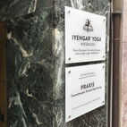 Hochwertiges Praxisschild aus weißem Plexiglas, montiert mit Edelstahl-Punkthaltern auf einer Marmorwand in Essen.