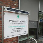 Solar-beleuchtetes Praxisschild aus weißem Acrylglas im modernen Edelstahl-Aufsteller für eine Klinik in Köln.